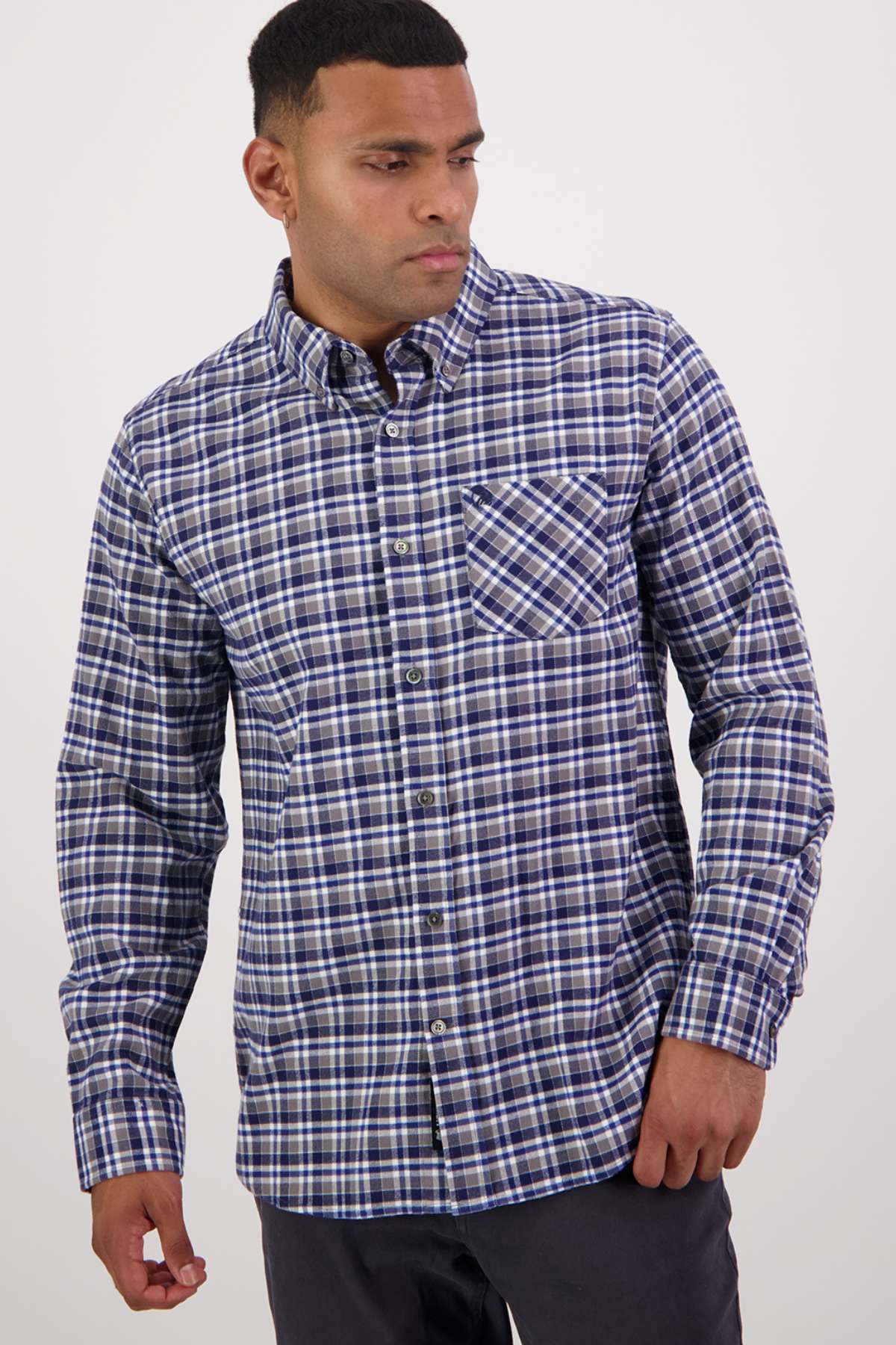 A man wears a Swanndri Wendon Shirt in blue, white, and black plaid with a classic fit and front chest pocket, standing against a plain light background.