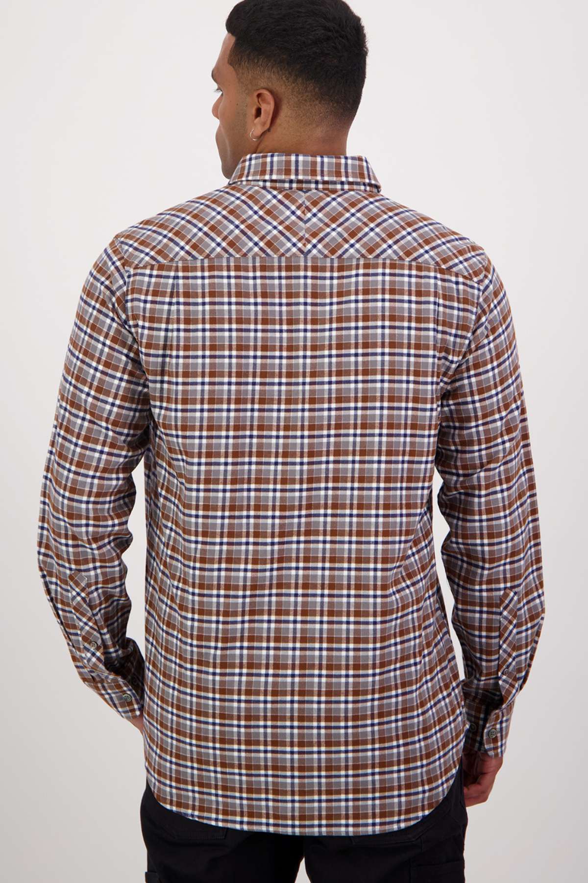 A man with short, dark hair is depicted from behind, wearing the Swanndri Wendon Shirt. This long-sleeved shirt features a brown, white, and blue plaid pattern and is crafted from 100% cotton in a classic fit. He stands against a plain white background.
