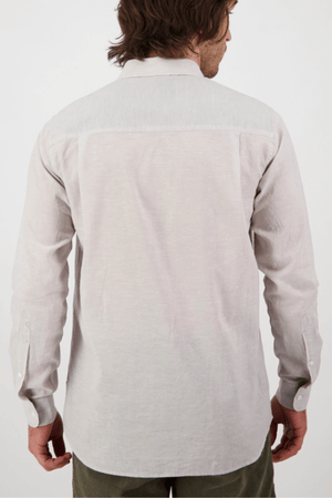 A brown-haired person with shoulder-length hair stands with their back to the camera, wearing a Swanndri Wolcott v2 Long Sleeve Shirt made from a linen cotton blend and dark green pants, set against a plain white background.