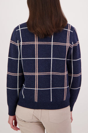 A person with shoulder-length brown hair is seen from the back, wearing the Swanndri Yasmin Check Womens Knit in navy blue with a white and beige windowpane pattern, paired with light-colored pants.