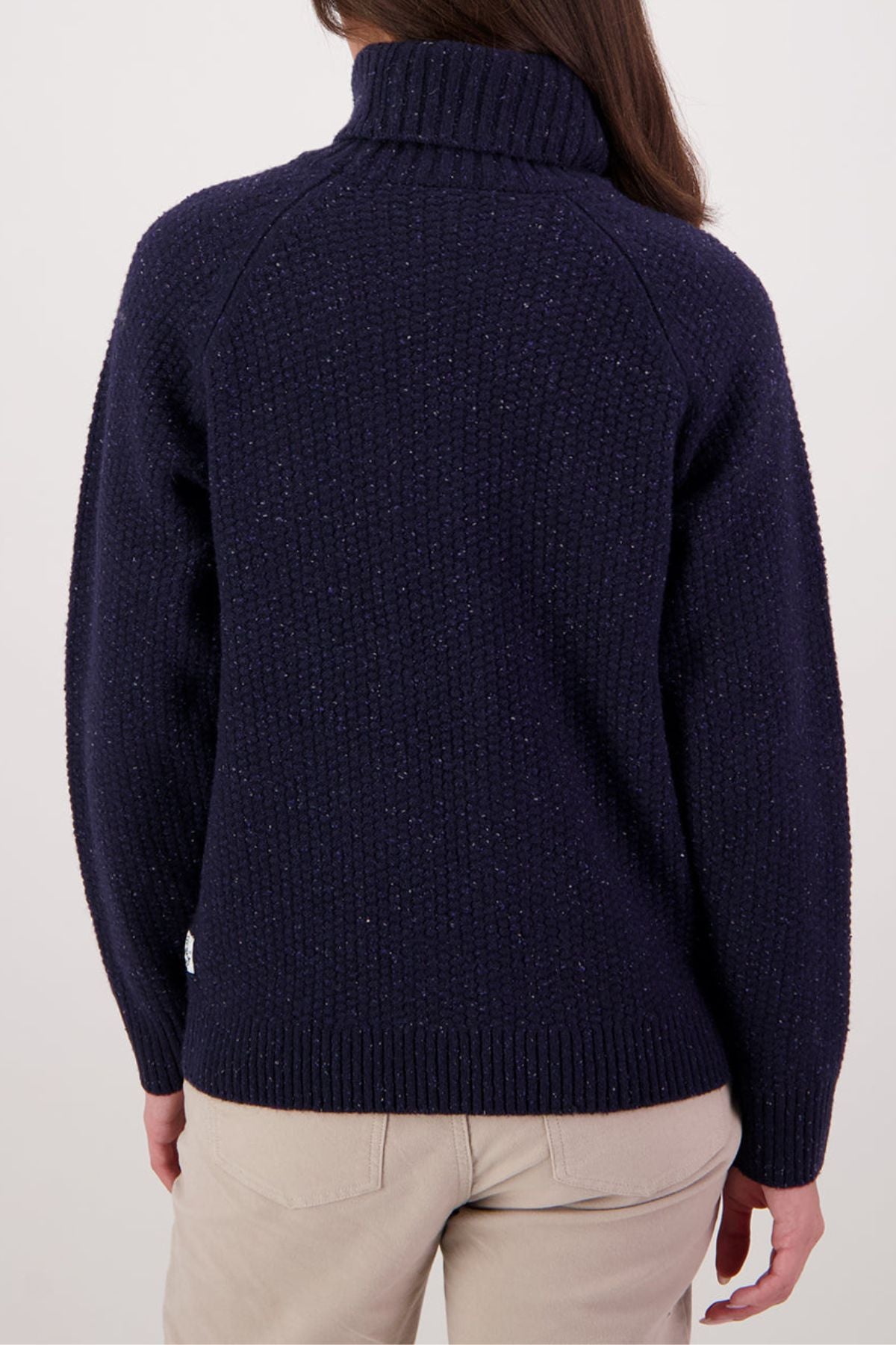 A person wears a dark navy Swanndri Lyttelton v2 Roll Neck Knit sweater with a high collar and beige pants, viewed from the back against a plain light background.
