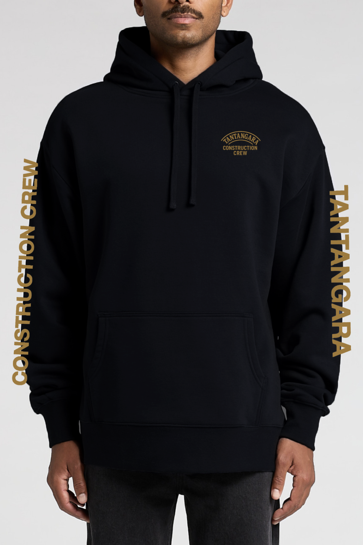 A man wears the Tantangara Construction Crew Hoodie PRE-ORDER in black with gold lettering on the chest and sleeves. This hoodie features a front pocket, drawstrings, and is available for pre-order.