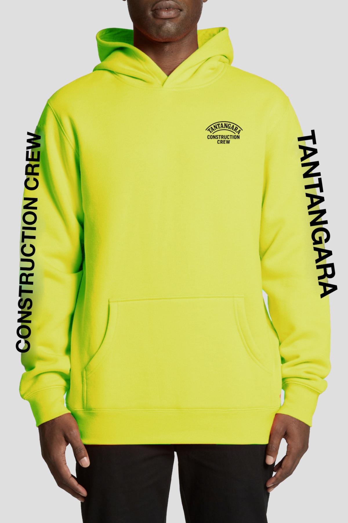 Wearing the Tantangara Construction Crew Hoodie PRE-ORDER in neon yellow with bold black “Tantangara Construction Crew” text on the chest and sleeves, a person stands against a plain, light background.