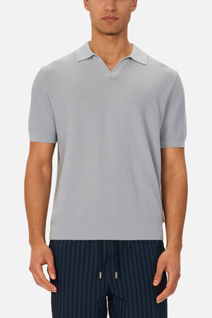 A man wearing the Industrie The Alicante Polo, a light gray knitted shirt with a small collar and v-neck, pairs it with dark blue pinstriped drawstring pants while standing against a plain white background.