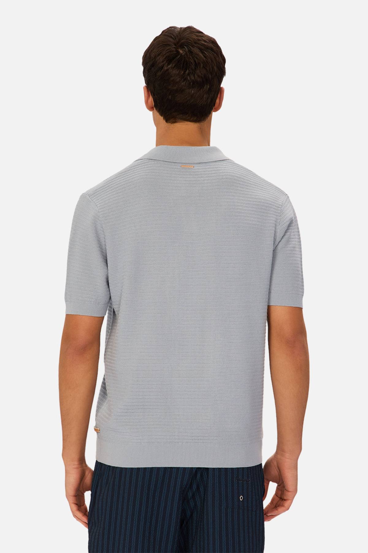 A man, seen from behind, wears the Industrie The Alicante Polo—a light gray men's cotton short-sleeve polo—with dark blue pinstriped pants against a plain white background.