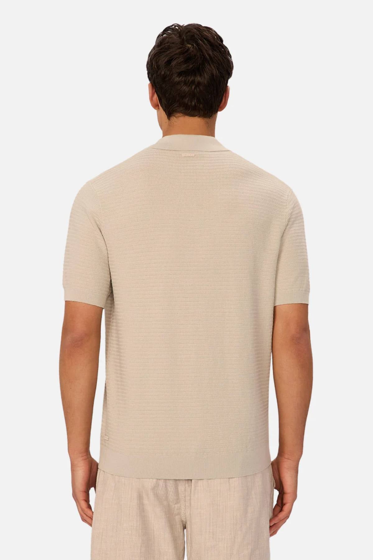 A man with short brown hair is seen from the back, wearing the Industrie The Alicante Polo in light beige and matching shorts against a plain white background.