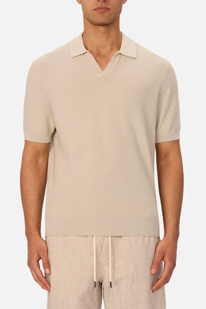 A man wears the Industrie The Alicante Polo in light beige with short sleeves and a notched collar, paired with matching beige drawstring shorts, standing against a plain white background.