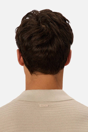 A person with short, dark brown hair is seen from behind wearing the Industrie The Alicante Polo, a textured beige knit with a small rectangular label at the neckline, set against a plain light-colored background.