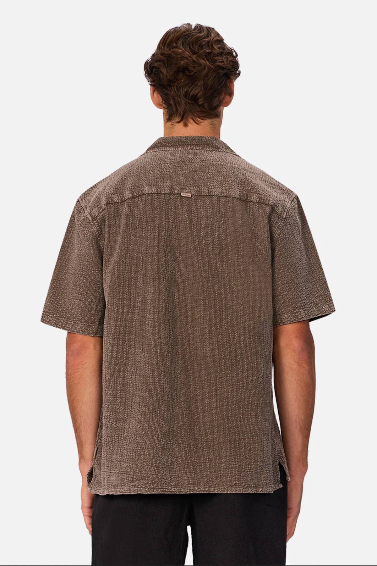 Seen from behind against a plain white background, a person with short brown hair wears the Industrie The Canyon Short Sleeve Shirt featuring a camp collar, paired with black pants.
