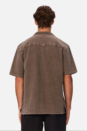 Seen from behind against a plain white background, a person with short brown hair wears the Industrie The Canyon Short Sleeve Shirt featuring a camp collar, paired with black pants.