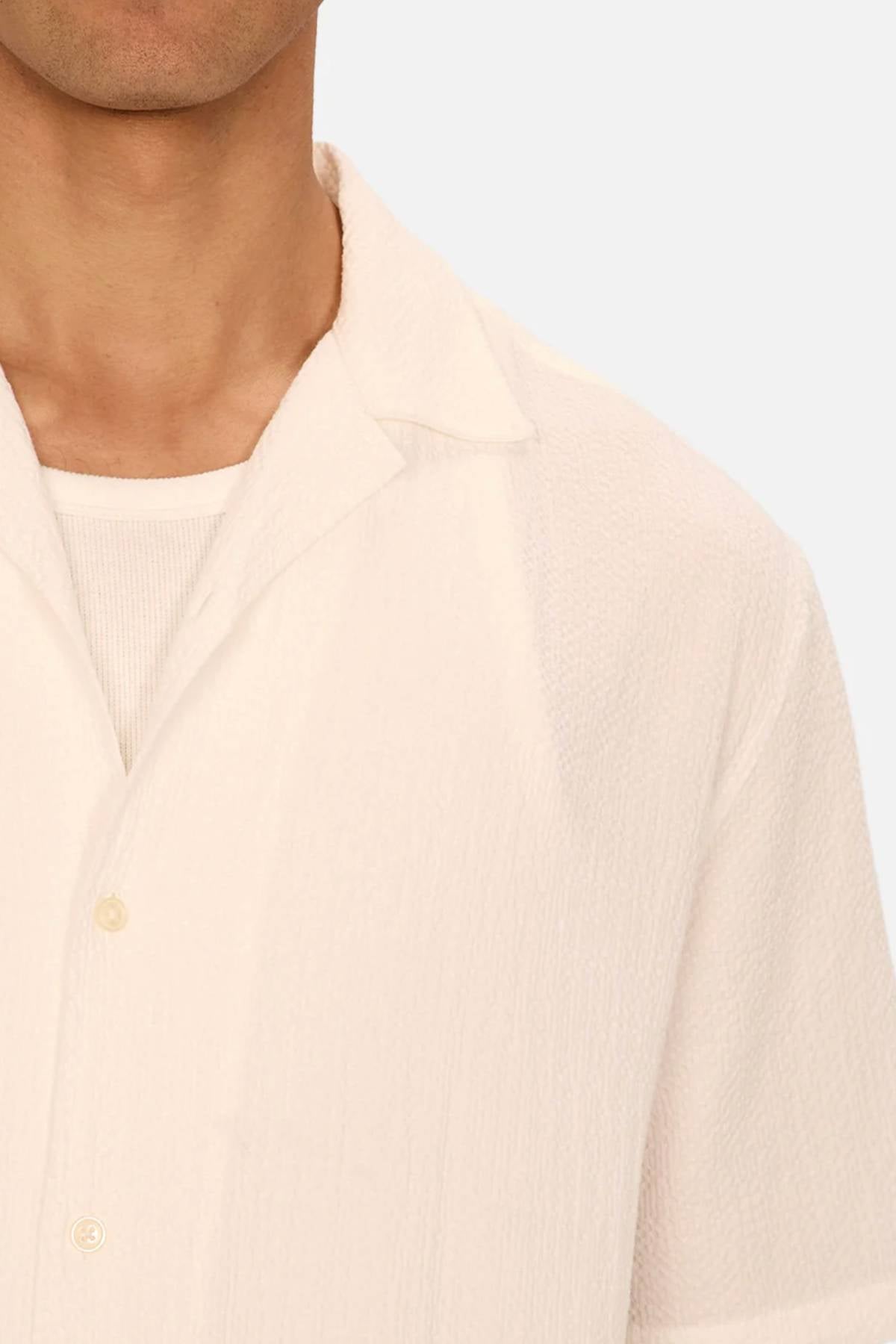 A close-up of a person wearing the Industrie The Canyon Short Sleeve Shirt, an off-white textured camp-collar style layered over a white ribbed undershirt, showing only the lower face, neck, and upper torso against a plain background.