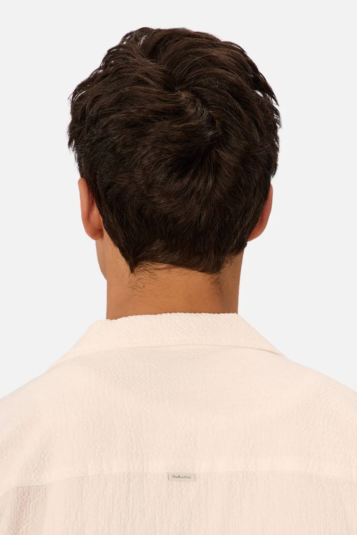 A person with short, dark brown hair is seen from behind wearing the Industrie The Canyon Short Sleeve Shirt, a textured white lightweight shirt with a classic collar, against a plain light background.