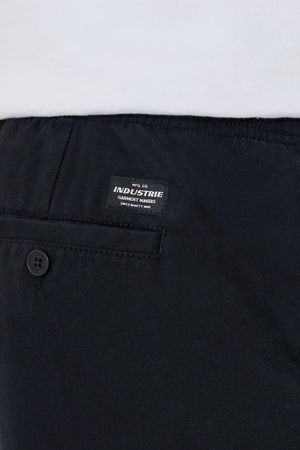 Close-up of the back of black Industrie The Dublin Short men’s summer shorts, featuring a buttoned pocket, a small rectangular "Industrie Garment Makers" label, and a white shirt tucked into the cotton-linen waistband.