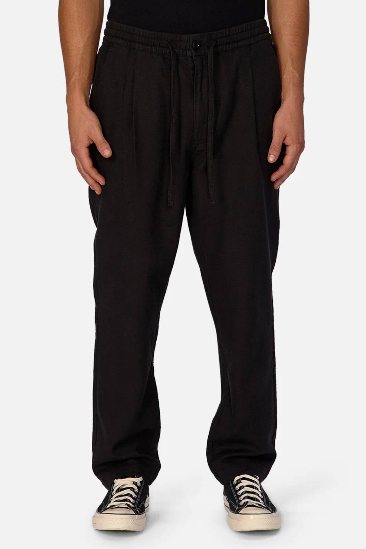 Someone wearing Industrie The Mallorca Pant—loose-fitting, breathable, with a drawstring waist—paired with a black shirt and black-and-white sneakers, stands against a plain light background.