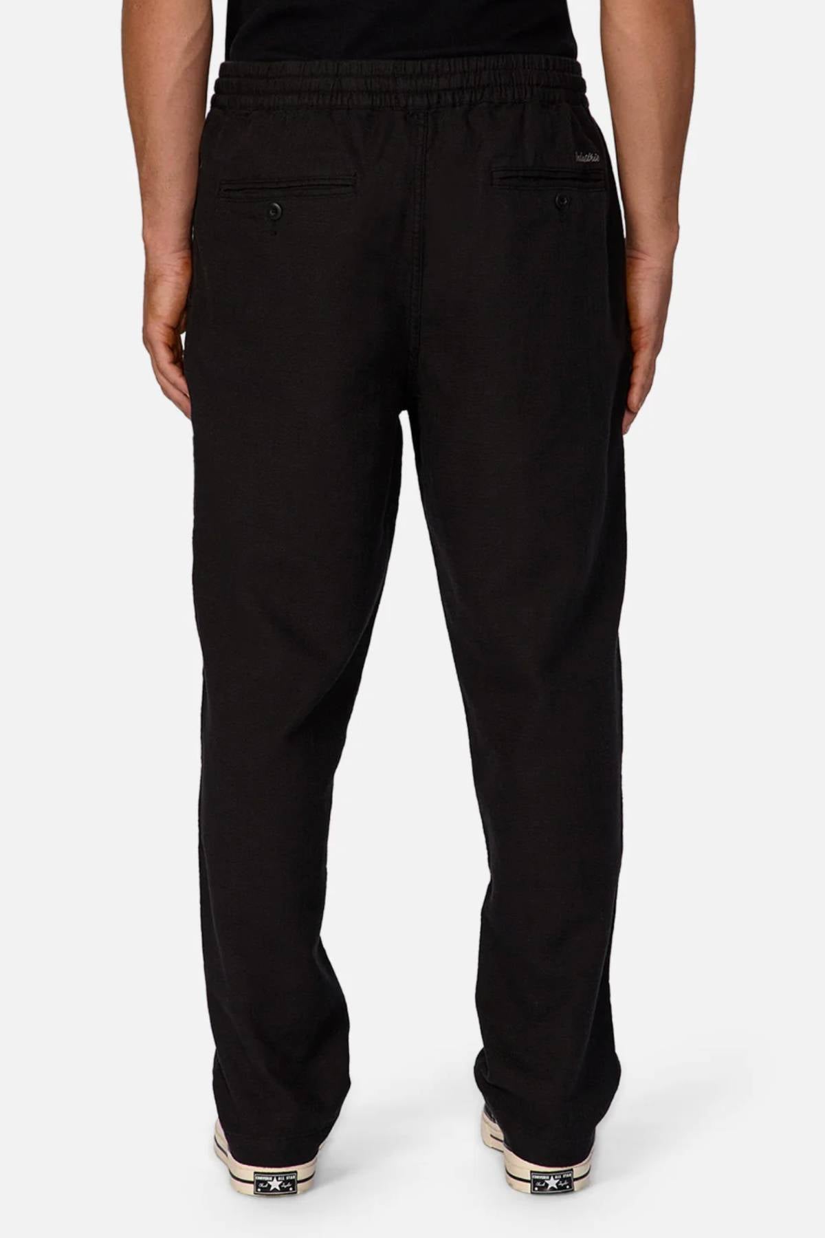 A person wears Industrie The Mallorca Pant in black, featuring breathable fabric, two back pockets, and an elastic waistband, shown from the back against a plain white background.