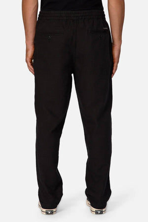 A person wears Industrie The Mallorca Pant in black, featuring breathable fabric, two back pockets, and an elastic waistband, shown from the back against a plain white background.