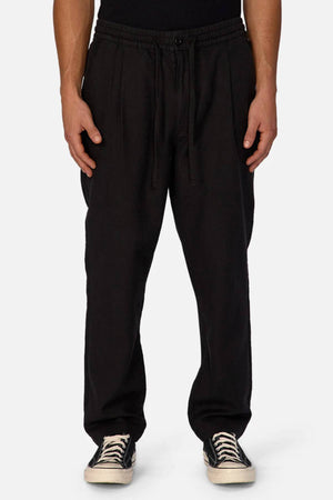 Someone wearing Industrie The Mallorca Pant—loose-fitting, breathable, with a drawstring waist—paired with a black shirt and black-and-white sneakers, stands against a plain light background.