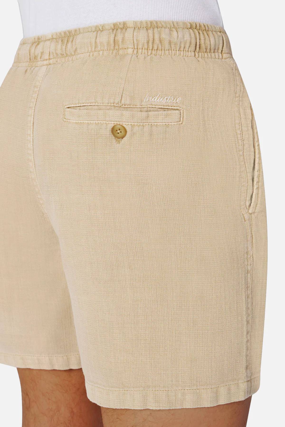 Close-up of a person wearing Industrie The Mallorca Short, men's cotton shorts with an elastic waistband, side pocket, back buttoned pocket, and white "ladrone" embroidery above the back pocket. Shirt is tucked in for a relaxed fit.