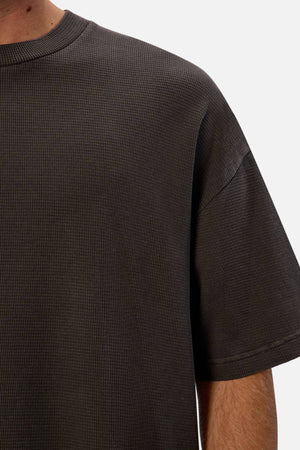 Close-up of a person wearing the dark gray Industrie The Marlon Tee, featuring short sleeves and textured waffle knit fabric. Only the upper torso, part of the left arm, and neck are shown against a plain white background.