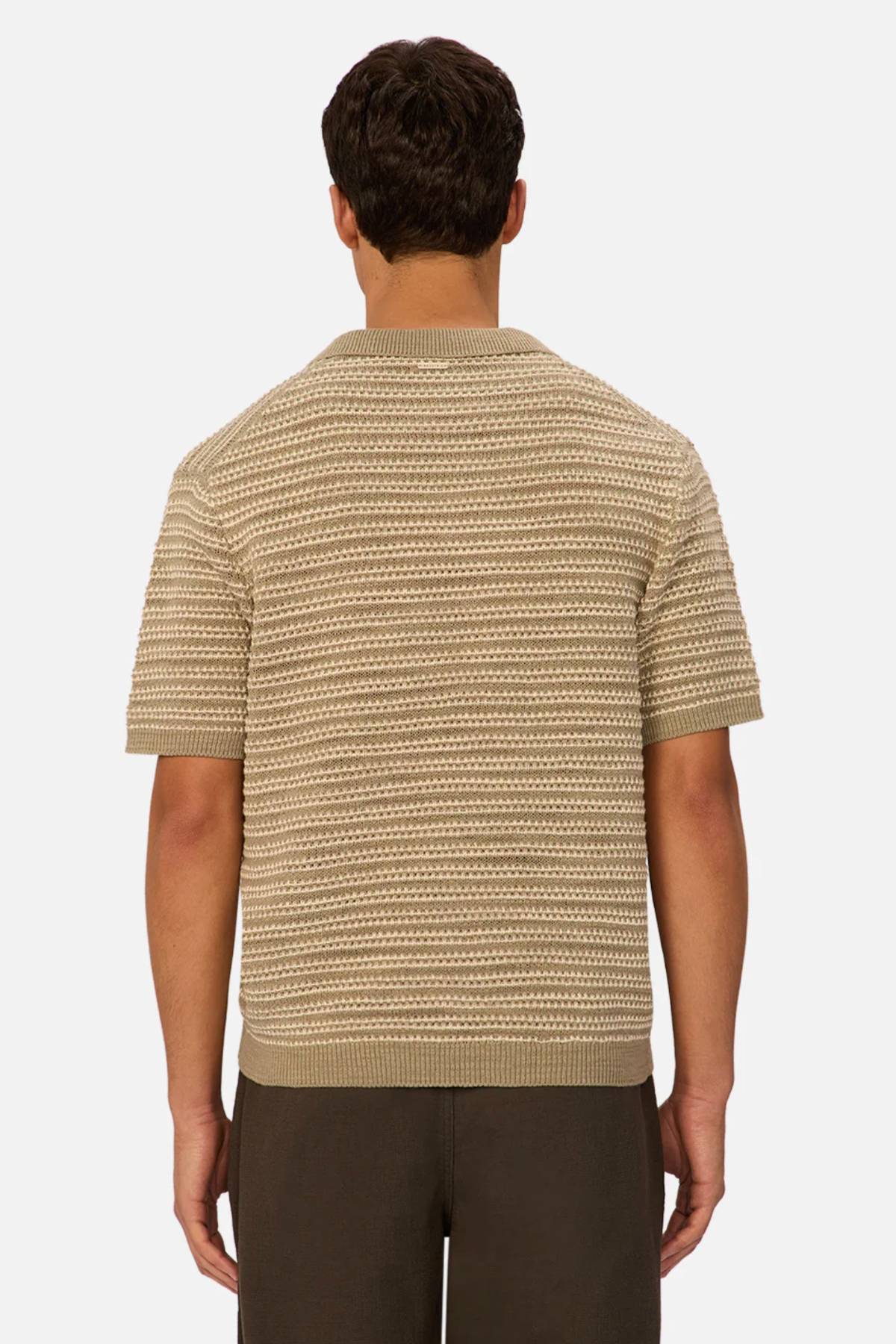 A man is seen from behind wearing an Industrie The Matera Polo, a heavyweight beige and cream striped 100% cotton knit, paired with dark pants, set against a plain white background.
