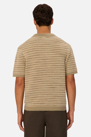 A man is seen from behind wearing an Industrie The Matera Polo, a heavyweight beige and cream striped 100% cotton knit, paired with dark pants, set against a plain white background.