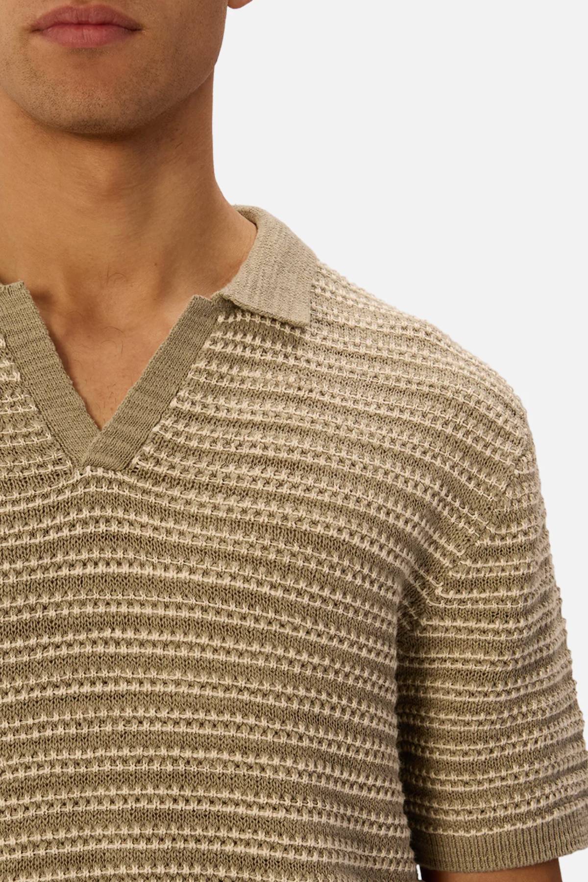 A close-up shows someone wearing the Industrie The Matera Polo, a short-sleeved beige and off-white striped shirt made from 100% cotton heavyweight knit with a V-neck collar. The person's face is partially out of frame.