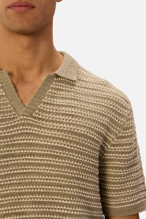 A close-up shows someone wearing the Industrie The Matera Polo, a short-sleeved beige and off-white striped shirt made from 100% cotton heavyweight knit with a V-neck collar. The person's face is partially out of frame.