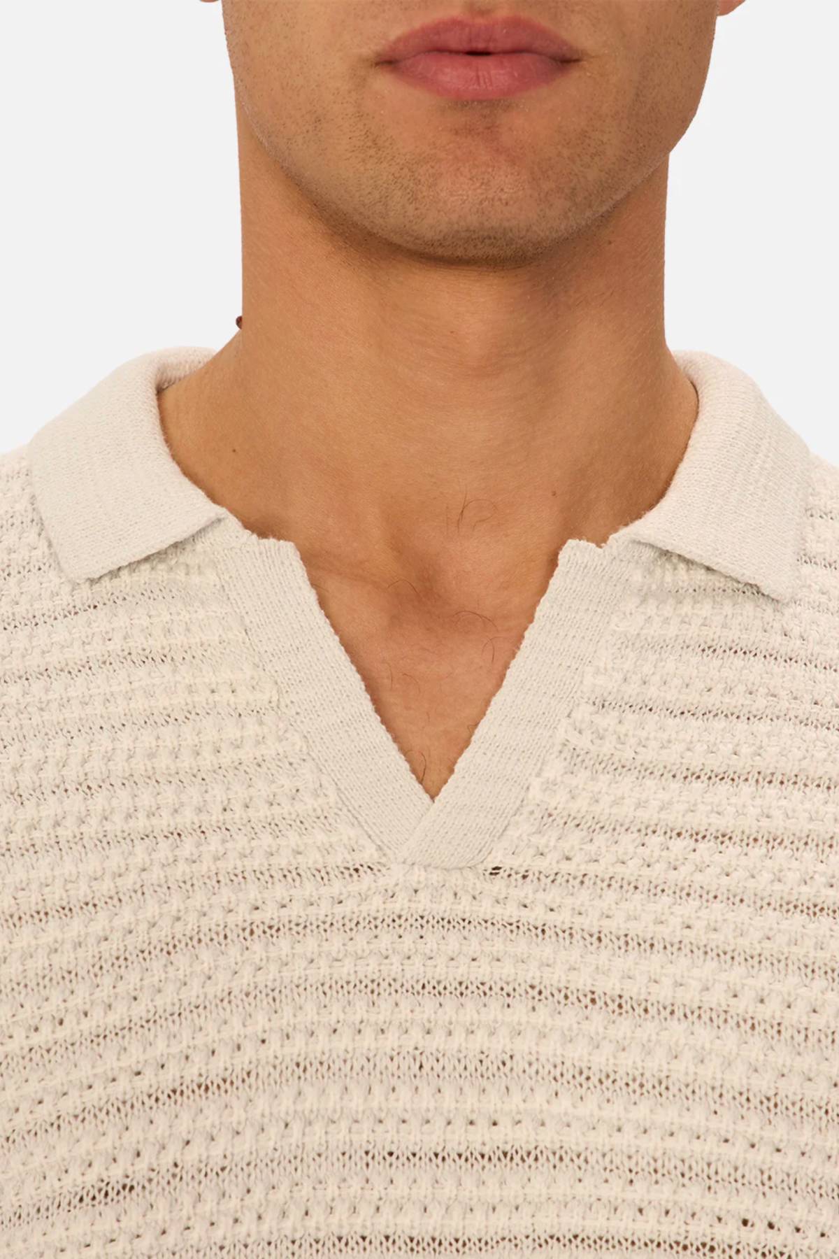 A close-up of a person wearing the Industrie The Matera Polo, a heavyweight off-white knit with textured finish, short collar, and V-shaped neckline revealing the lower face and neck against a plain background.