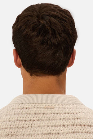 A person with short, dark brown hair is seen from behind wearing the Industrie The Matera Polo, a heavyweight, textured knit in cream. The backdrop is plain and light-colored.