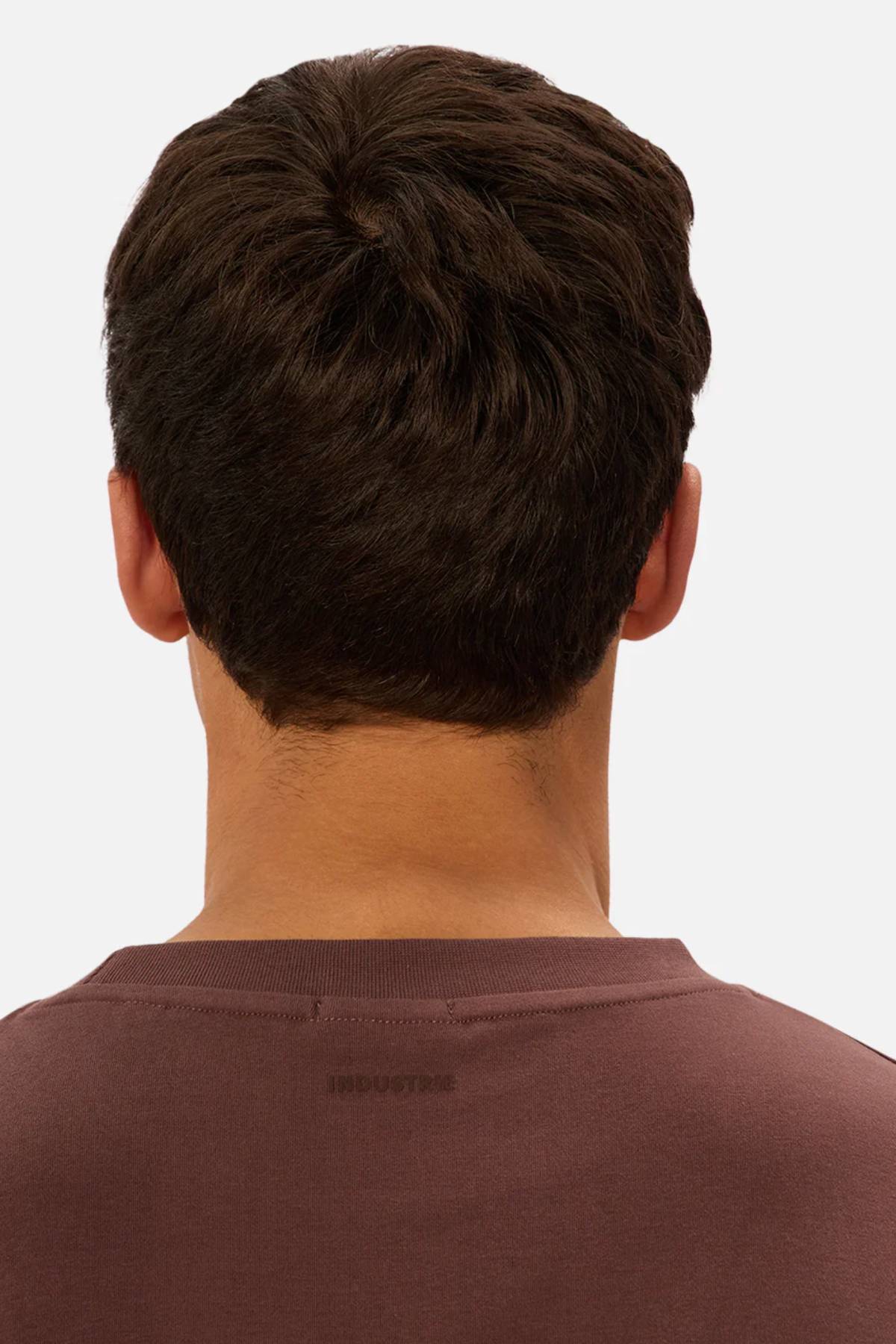 A person with short, dark brown hair is seen from behind wearing an oversized maroon Industrie The Newport Tee against a plain, light background.