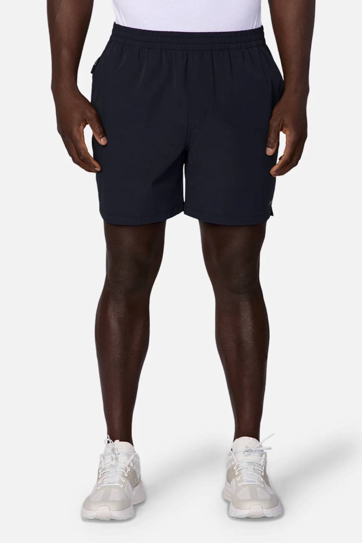 A person is shown from the shoulders down against a plain background, wearing a white shirt, white sneakers, and Industrie The Owens Short—black quick-drying shorts with an elasticised waistband.