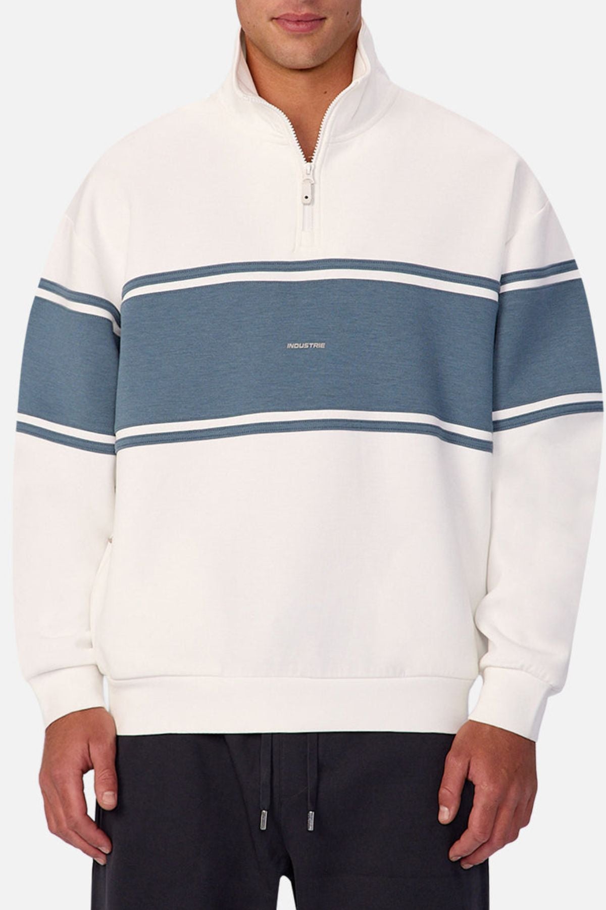 Wearing the Industrie The Tech Southend Track Top—a white pullover with a blue stripe, thin white lines, half-zip collar, and small center text—offers a casual look. The tech fabric ensures comfort. Pairs well with black pants.