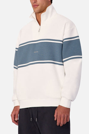 Wearing the Industrie The Tech Southend Track Top in white with blue chest and sleeve stripes, paired with dark pants. Only the lower face and torso are shown, creating a stylish casual look.