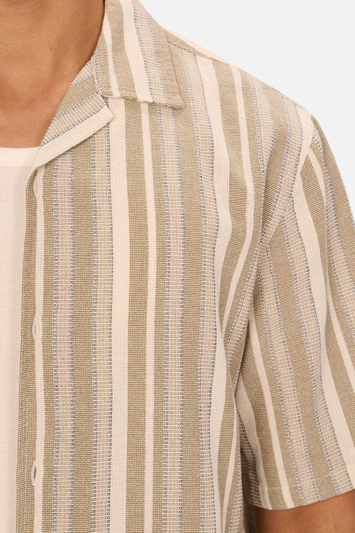 A close-up of a person wearing the Industrie The Textured Livorno Short Sleeve Shirt, featuring beige and white vertical stripes, layered over a white ribbed top.