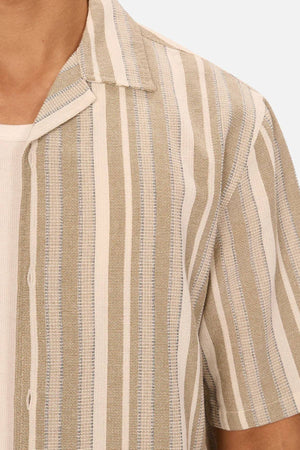 A close-up of a person wearing the Industrie The Textured Livorno Short Sleeve Shirt, featuring beige and white vertical stripes, layered over a white ribbed top.
