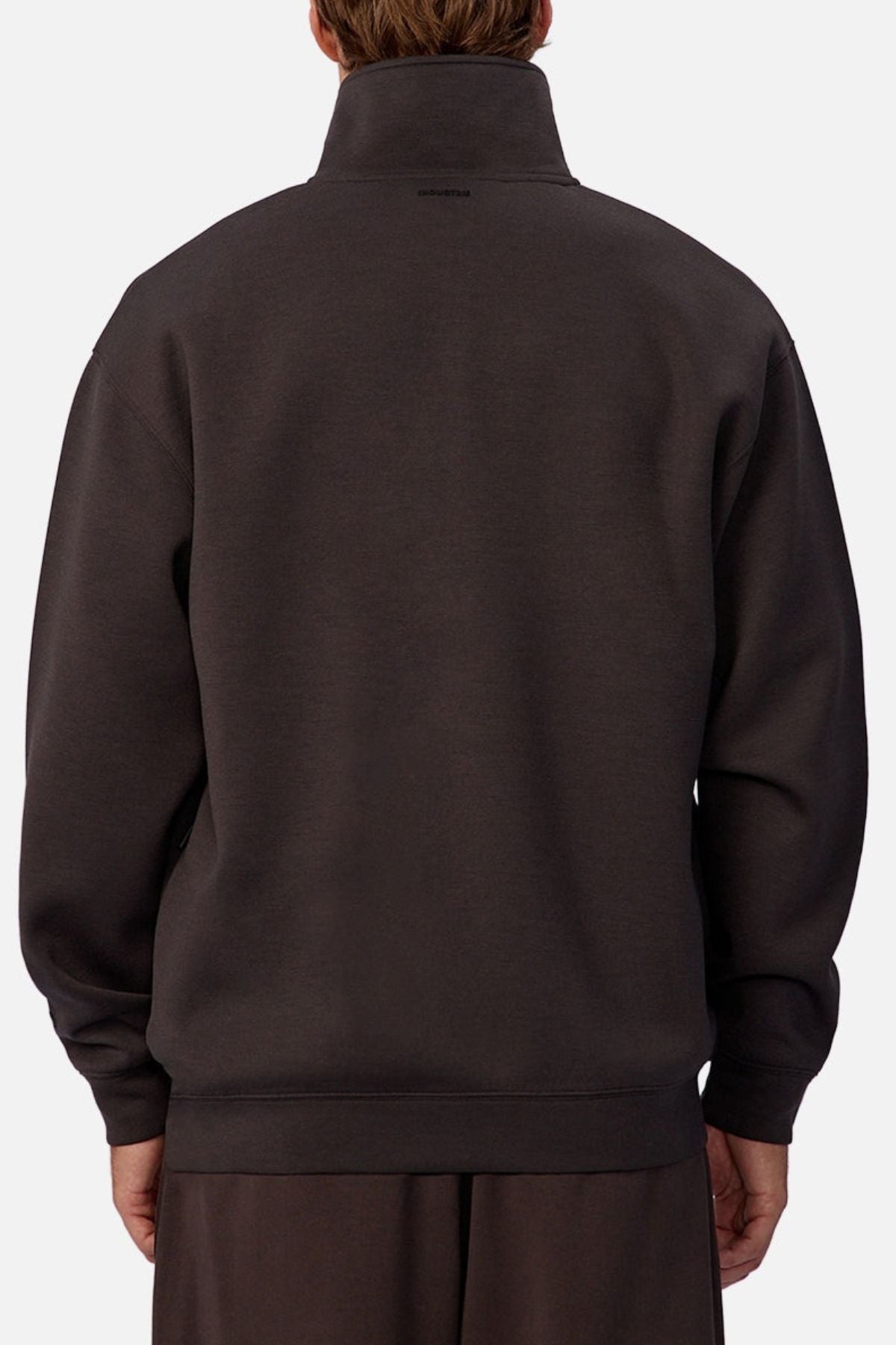 Someone is seen from behind wearing the Industrie The Tech Staunton Track Top, a loose-fitting dark gray athletic pullover with the collar up and hands relaxed at their sides against a plain, light background.