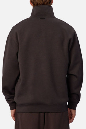 Someone is seen from behind wearing the Industrie The Tech Staunton Track Top, a loose-fitting dark gray athletic pullover with the collar up and hands relaxed at their sides against a plain, light background.