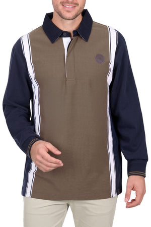 A man wears the Thomas Cook Travis Rugby, featuring a brown front panel, navy blue sleeves, white vertical stripes, and a dark collar. He smiles and poses with one hand slightly raised.