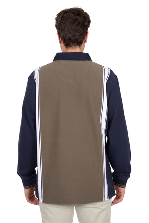 A man with short brown hair wears light pants and the Thomas Cook Travis Rugby, featuring navy long sleeves, an olive-green back panel, and vertical white and navy stripes.