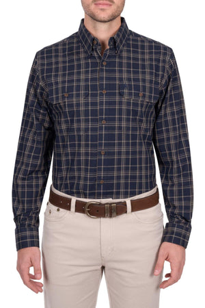 A man wears the Thomas Cook Adam Shirt—navy blue and tan plaid, 100% cotton, long sleeves—with light beige pants and a brown belt. The photo shows him from shoulders to mid-thigh, facing forward.
