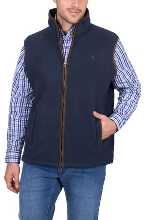A man wearing a blue checkered shirt, Thomas Cook Adrian Vest, and blue jeans stands with one hand in his pocket against a white background.