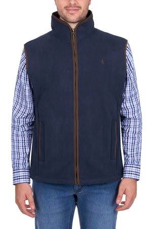 A man wearing the Thomas Cook Adrian Vest in navy blue over a blue and white checkered shirt with blue jeans, standing against a white background.