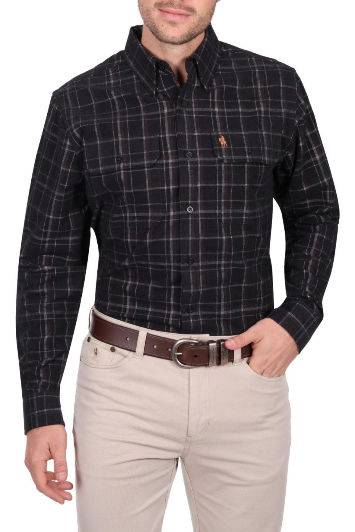 A man wears a black and white Thomas Cook Ben Thermal Shirt tucked into light beige pants with a brown belt, standing with one hand in his pocket against a white background.