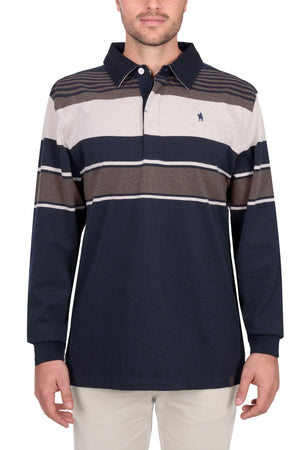 A man wears the Thomas Cook Bryan Stripe Rugby, a long-sleeve collared shirt with navy, beige, and brown stripes and a small embroidered logo on the chest, paired with light-colored pants.