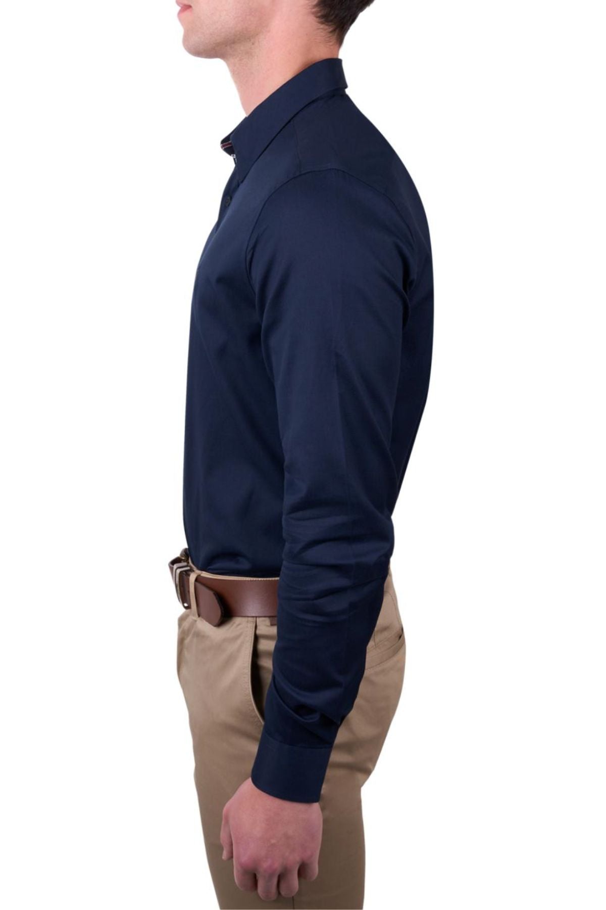 A man stands in profile, facing left, wearing the Thomas Cook Callum Tailored Shirt in navy blue with beige pants and a brown belt, his hand relaxed at his side.