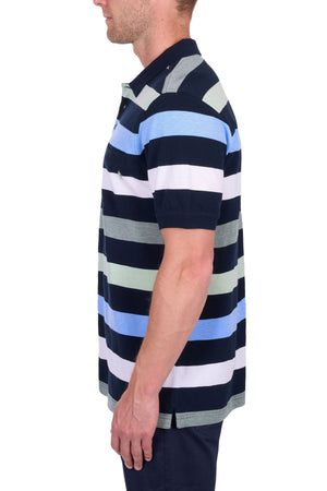 A man is seen in profile wearing the Thomas Cook Charles Polo, a 100% cotton pique polo with multi-coloured stripes, paired with dark shorts, set against a plain white background.