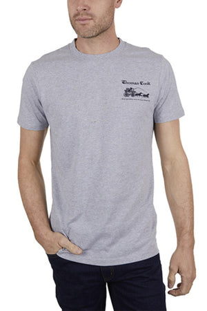 A man wears the Thomas Cook Coach Tee, a light grey cotton jersey with "Thomas Cook" and a graphic on the chest, paired with dark jeans as he stands casually, one hand in his pocket.