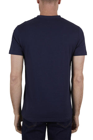 A man is seen from behind wearing the Thomas Cook Coach Tee, a plain dark blue cotton jersey t-shirt, paired with dark jeans against a white background.