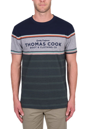 A man wearing the Thomas Cook Dion Tee, a multi-colour striped 100% cotton jersey with "Thomas Cook Boot & Clothing Co" on the front, paired with beige pants and standing against a white background.