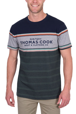 A person wears the Thomas Cook Dion Tee, a 100% cotton jersey featuring multicolour stripes and “Thomas Cook Boot & Clothing Co” on the chest, paired with light-colored pants.